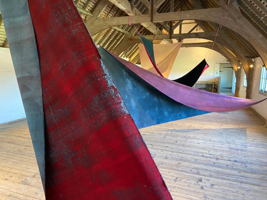 Stained canvases in deep red, blue and magenta suspended and twisted through the roof space of a timber barn. Flight, 2021, by Emma Hurst.