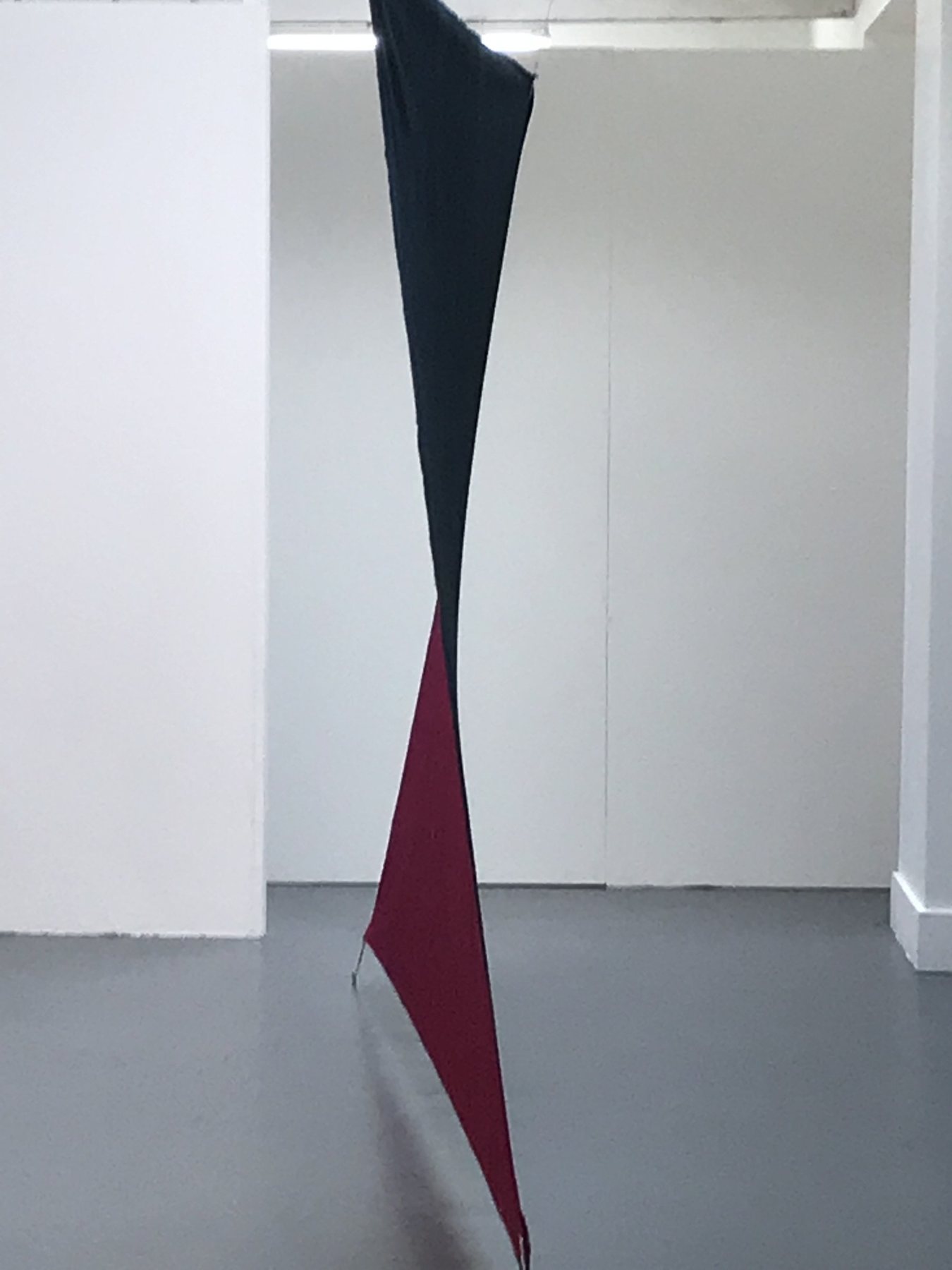 A single length of navy and deep red canvas twisted as it falls from ceiling to floor in a white room. Untitled, 2019 by Emma Hurst.